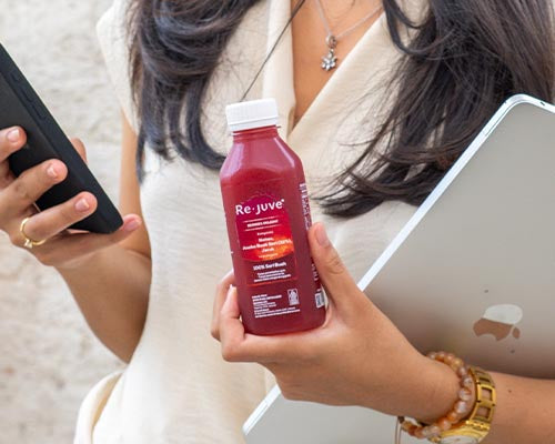 working woman holding a rejuve bottle with a phone and laptop